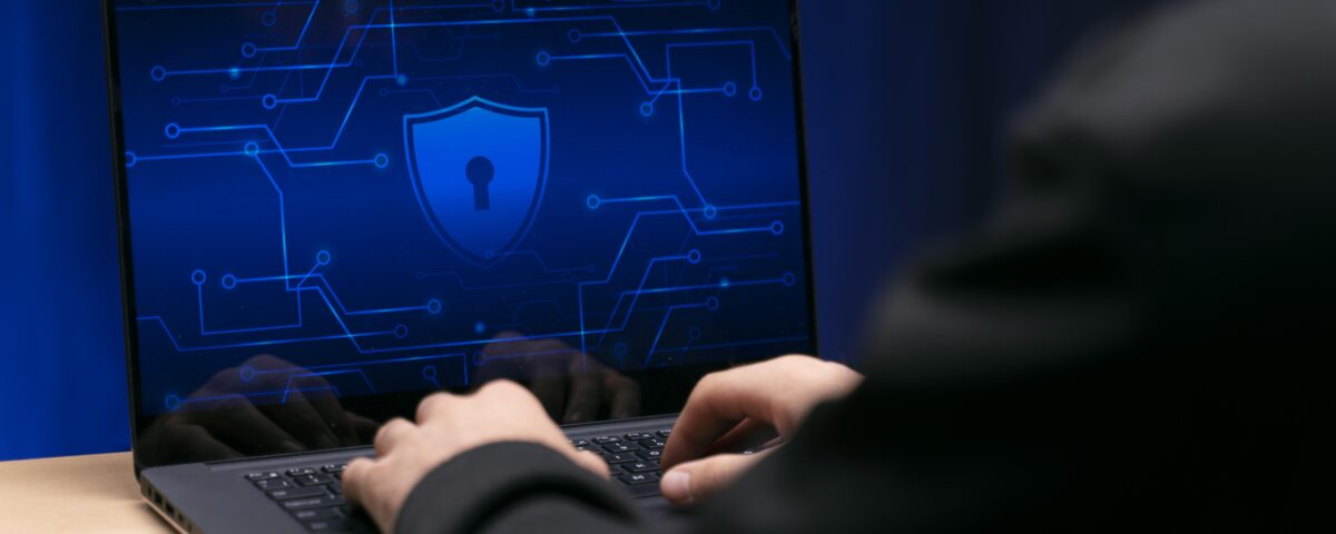 Osoba pracuje na laptopie z wyświetlonym symbolem ochrony danych i zamkniętą kłódką na niebieskim tle cyfrowym.