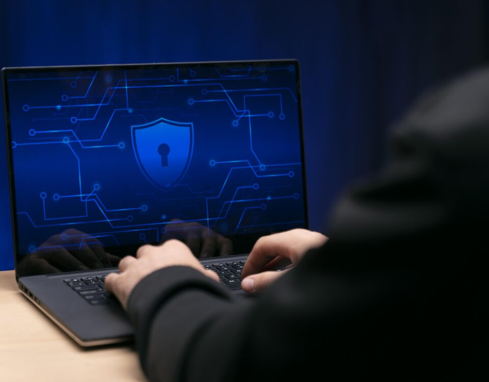 Osoba pracuje na laptopie z wyświetlonym symbolem ochrony danych i zamkniętą kłódką na niebieskim tle cyfrowym.